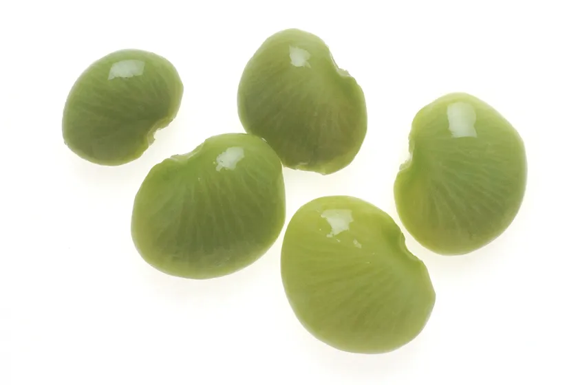 Five fresh green lima beans on a white background before cooking